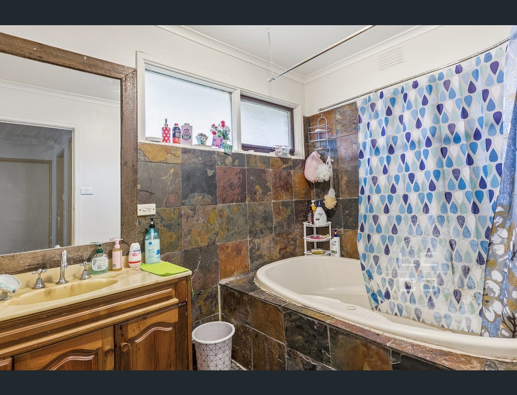 Bathroom with timber vanity, mirror and corner bath with shower curtain